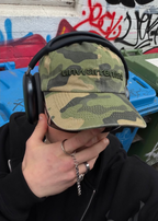 Close-up of the embroidered Unwarrented logo on the camo field cap